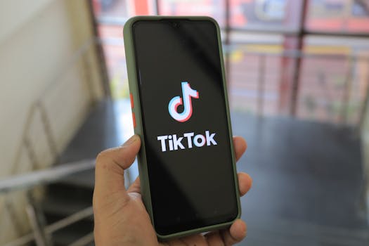 Hand holding a smartphone showing the TikTok app screen in an indoor setting.