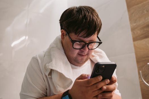 Man with Down syndrome wearing glasses focused on his smartphone indoors.