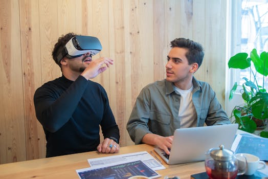 Two colleagues engage in a tech-savvy business meeting using virtual reality and laptops indoors.