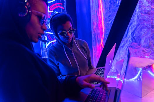 Two individuals working on laptops in a neon-lit setting, emphasizing technology and teamwork.